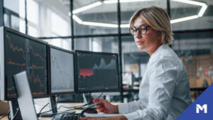 Office worker in white shirt watches over stocks on multiple monitors