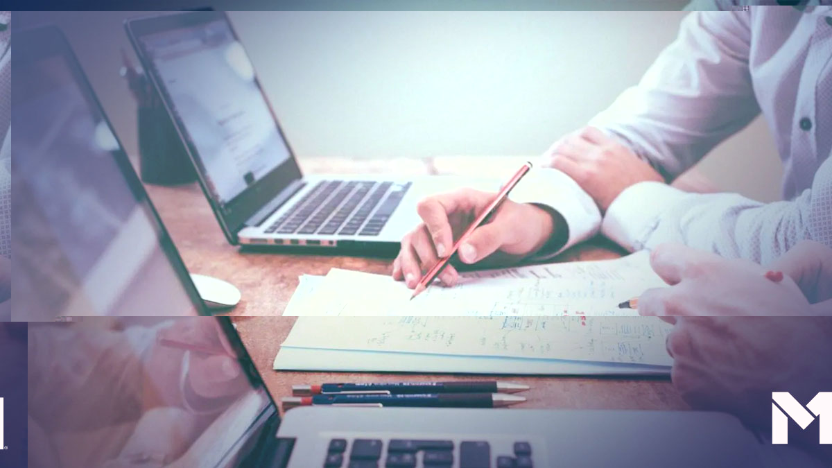 Two people writing on a document with their laptops open beside them.