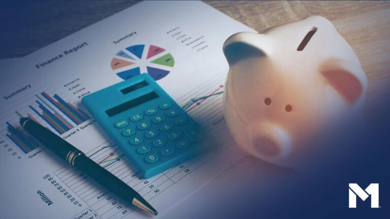 A desk with a piggy bank, a calculator, and a pen sittig on top of a financial report showing charts and graphs.